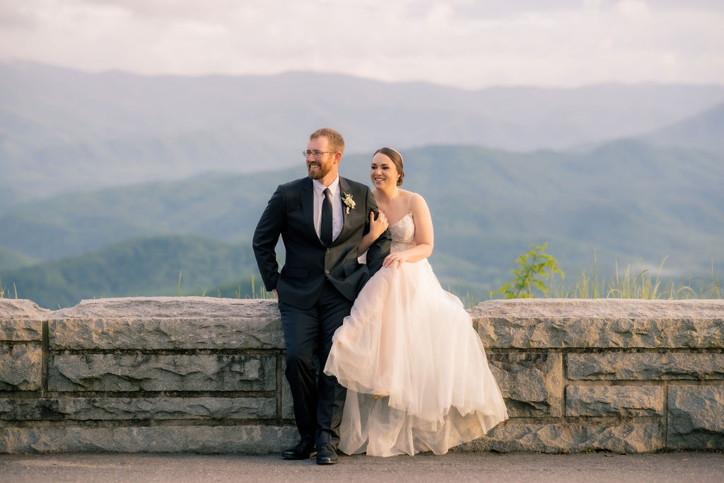 bride and groom sitting together on a road divide and holding each other while looking at the tree line