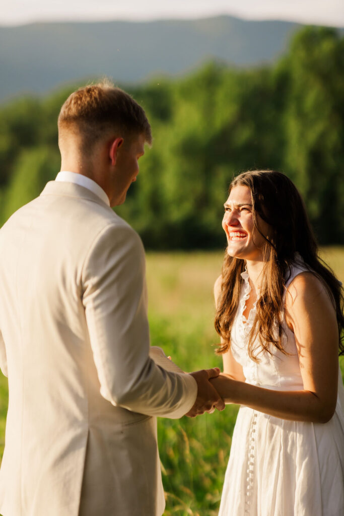 candid wedding photo of bride laughing at sunset while holding her grooms hands