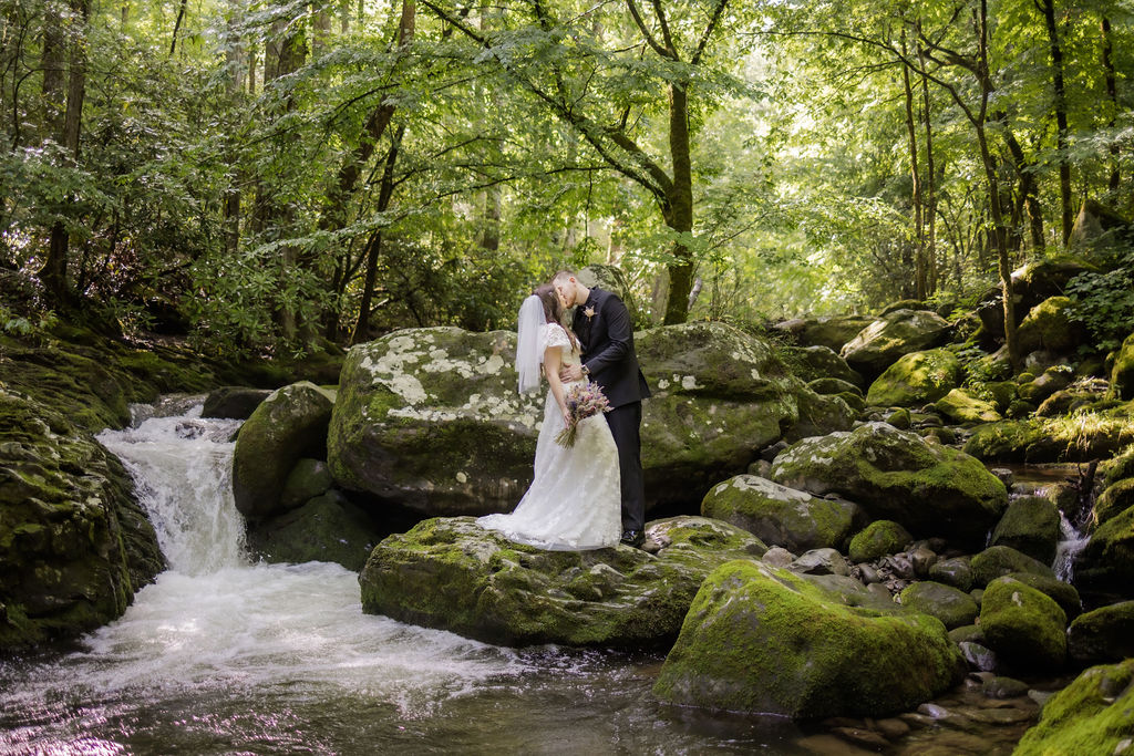 groom dips his bride backwards and kisses her while standing on a waterfall captured by photographers in gatlinburg tn