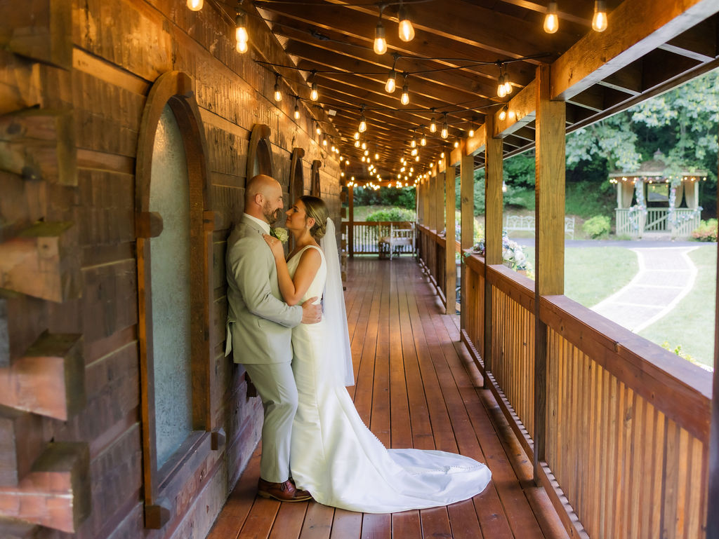 A romantic moment between the bride and groom captured on the wooden wraparound porch of Chapel in the Glen. The warm glow of string lights creates a magical ambiance, illuminating the rich wooden textures of the chapel’s rustic architecture. In the background, a beautifully decorated outdoor gazebo peeks through lush greenery, enhancing the cozy charm of this Gatlinburg elopement setting.