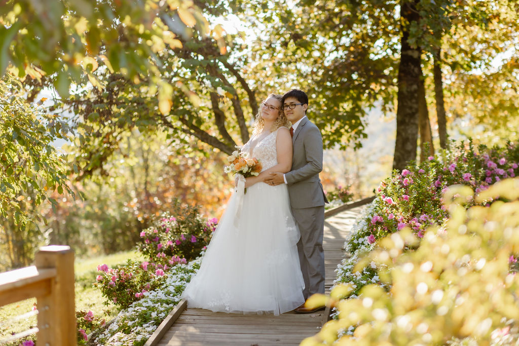 smoky mountain elopement with bride and groom standing on a path in a wooded garden with the groom holding his brides waist and smiling as she leans back into him