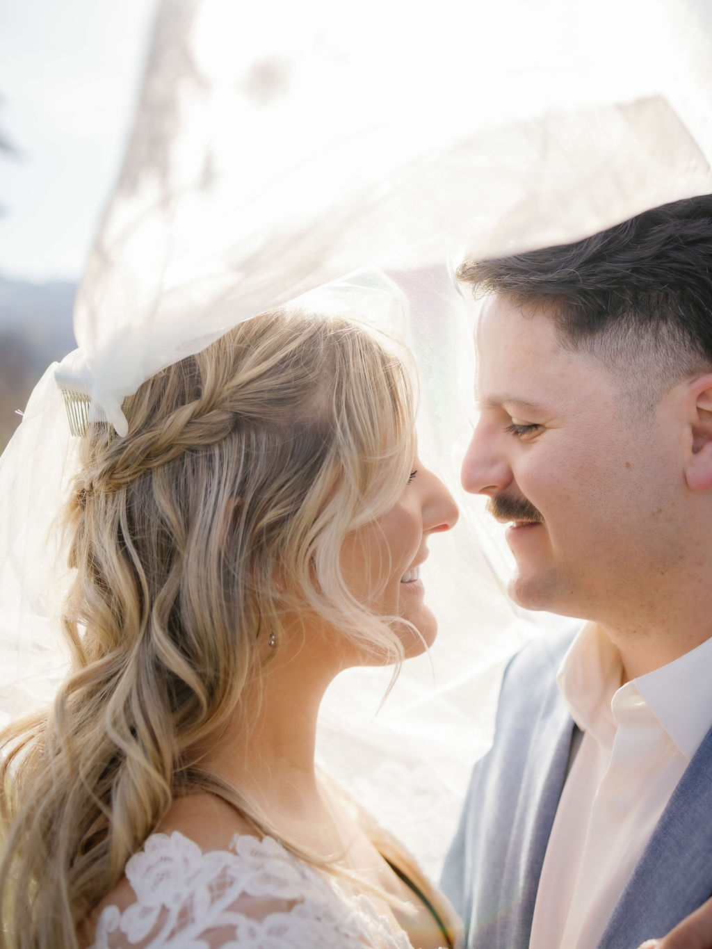 romantic wedding photos by Gatlinburg photographer with bride and groom standing under the brides veil that illuminates the couple in the sunset as they stand close and smile at each other for their Gatlinburg elopement