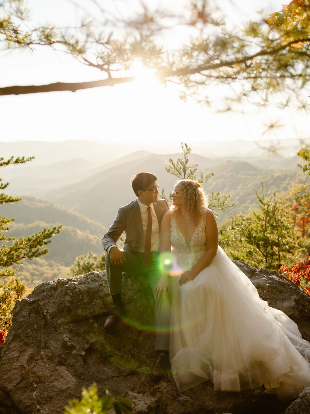 couple sits on a large rock at the Foothills, gazing into each other's eyes as the sun sets over the Smoky Mountains