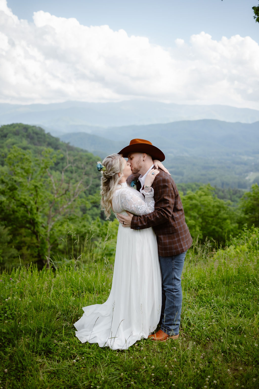 Bride and groom sharing a kiss in a grassy mountain clearing with layers of blue ridges in the distance during their smoky mountain elopement, photographed by Gatlinburg photographer.