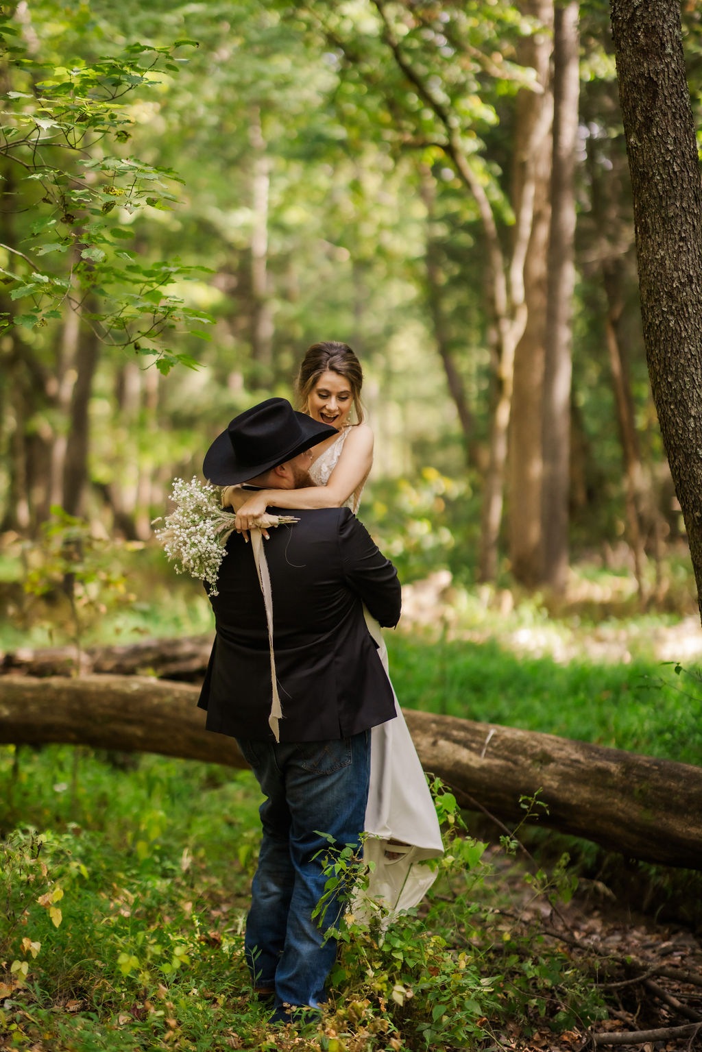 Groom lifts bride in a joyful embrace during their Cades Cove elopement, surrounded by a sunlit forest, captured by a Gatlinburg photographer.