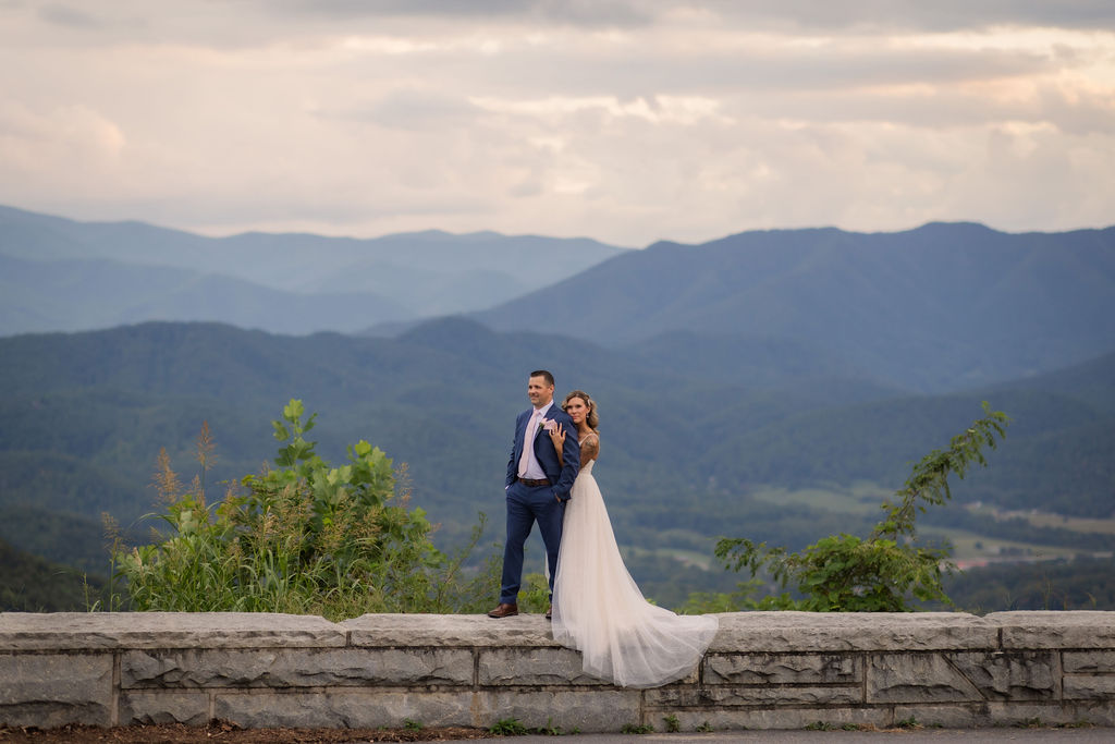 Bride and groom standing on a stone ledge overlooking mountain views during a smoky mountain elopement, celebrating eloping to Gatlinburg, photographed by a Gatlinburg photographer.