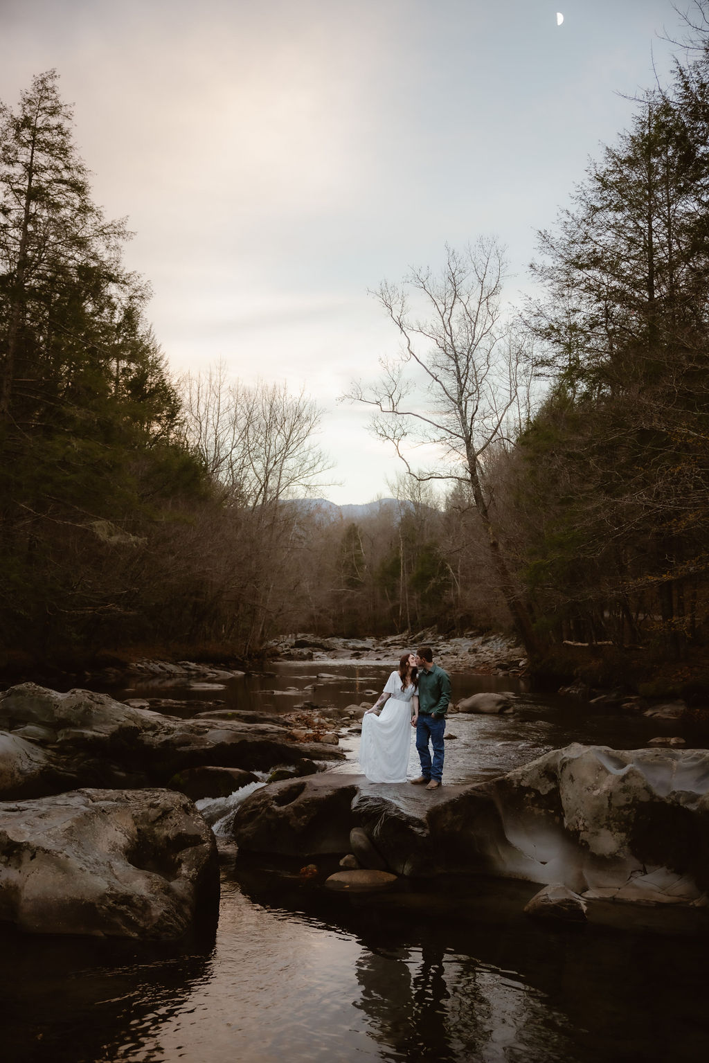 Bride and groom sharing a kiss on the rocks over the water at sunset in Greenbrier Gatlinburg Tennessee, a dreamy scene for couples eloping to Gatlinburg.