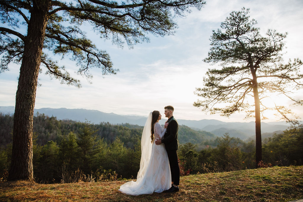 Winter Smoky Mountains elopement with a bride and groom standing together between two tall pine trees as the sun sets over the mountains, captured by Gatlinburg photographer.