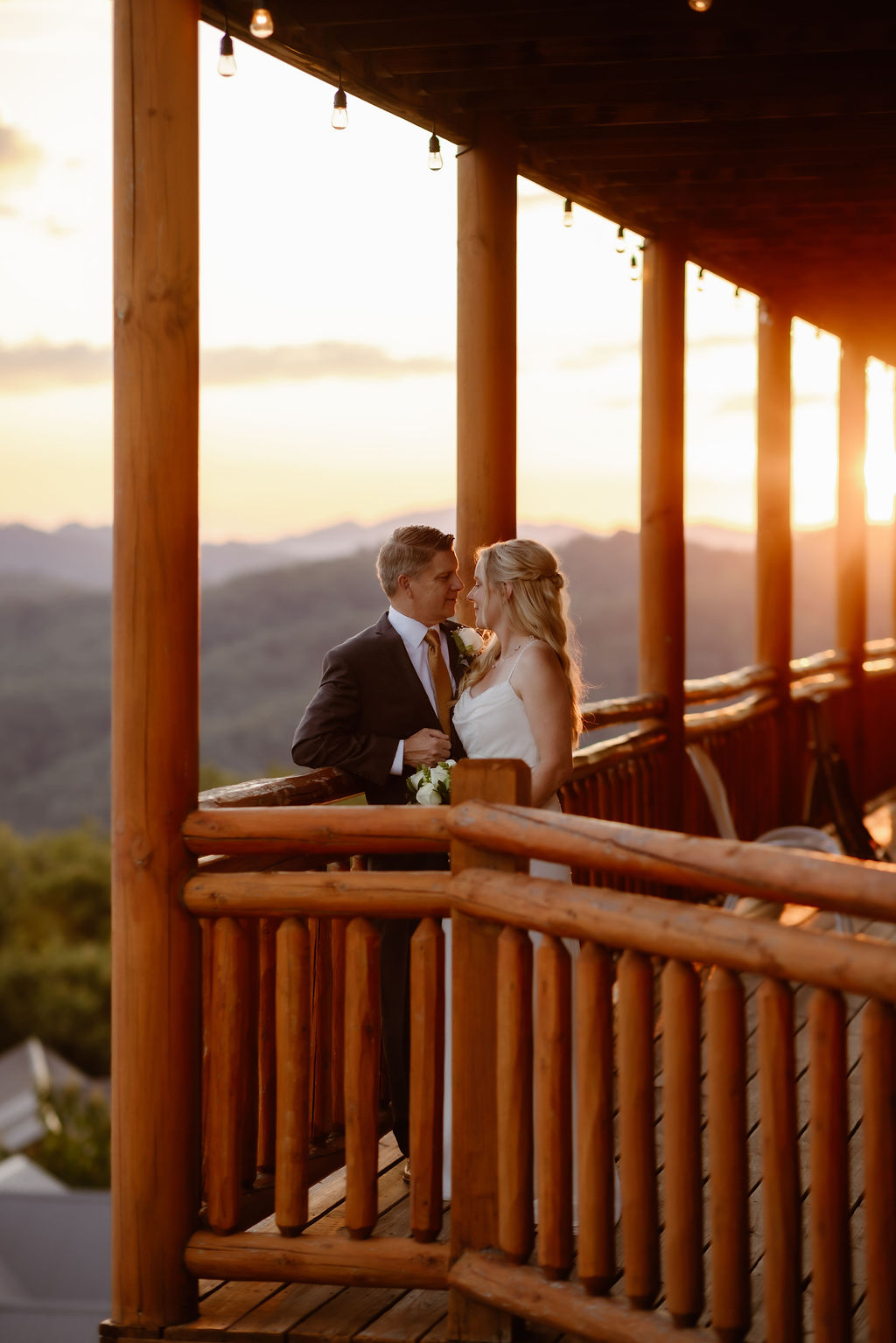 Eloping to Gatlinburg with a bride and groom sharing a moment on a wooden cabin balcony at sunset, surrounded by Smoky Mountain views during a cabin wedding Gatlinburg TN.