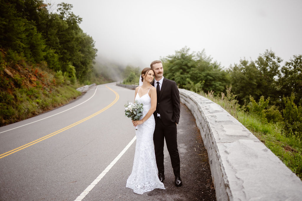 Wide shot of couple standing side by side on a foggy scenic road, surrounded by greenery during a Gatlinburg elopement.