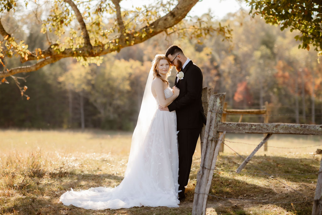 Bride and groom stand together near a rustic wooden fence under golden trees, showcasing a peaceful setting ideal for eloping to Gatlinburg and scenic elopement planning.