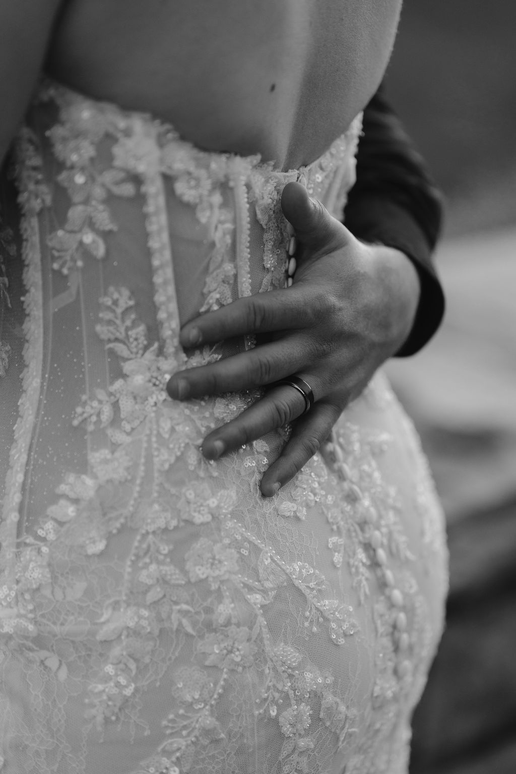 This black and white close-up beautifully captures the intimate connection between the couple. The groom’s hand, gently resting on the intricate lace of the bride’s gown, highlights the delicate details of the fabric and the tenderness of the moment. It’s a quiet, powerful image that speaks of love, support, and a lifelong promise.