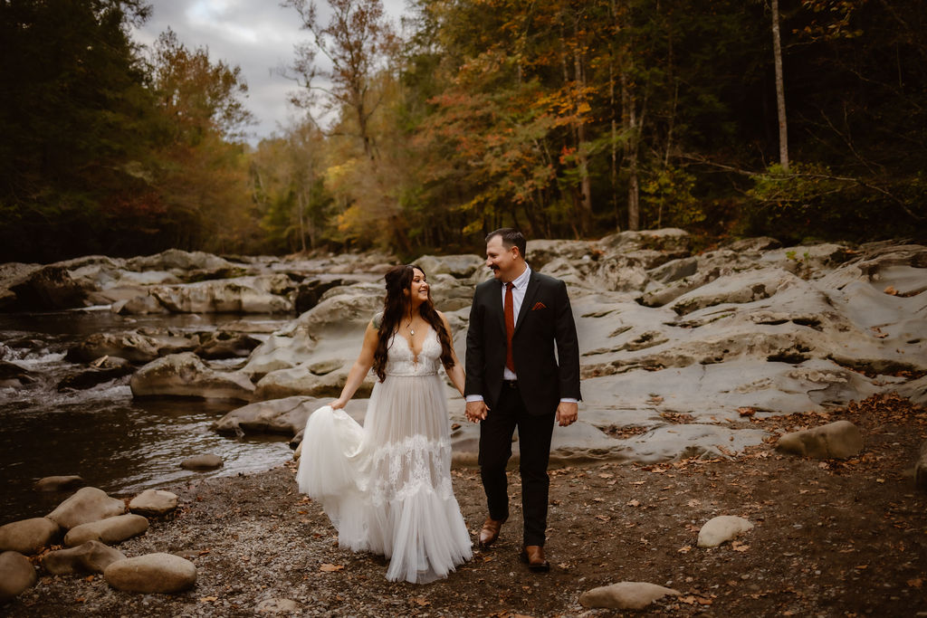 Couple holding hands along a rocky riverbank while eloping to Gatlinburg during a winter elopement, capturing a romantic outdoor adventure in the Smoky Mountains.