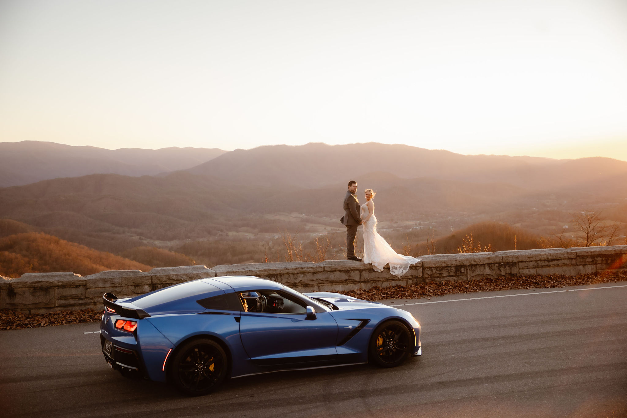 Blue sports car parked along the Foothills Parkway overlook as a bride and groom pose together during their luxury Smoky Mountain elopement to Elope to Gatlinburg.