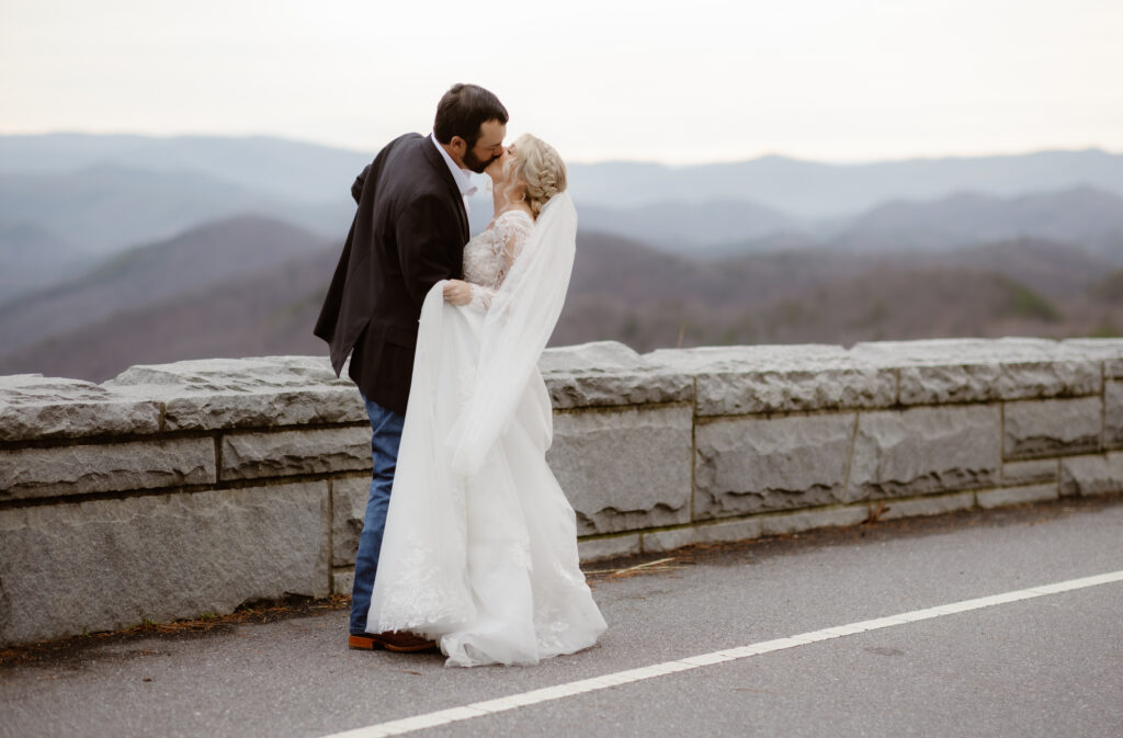 Bride and groom sharing a kiss beside a Smoky Mountain overlook during their eloping to Gatlinburg wedding portraits with mountain views in the background