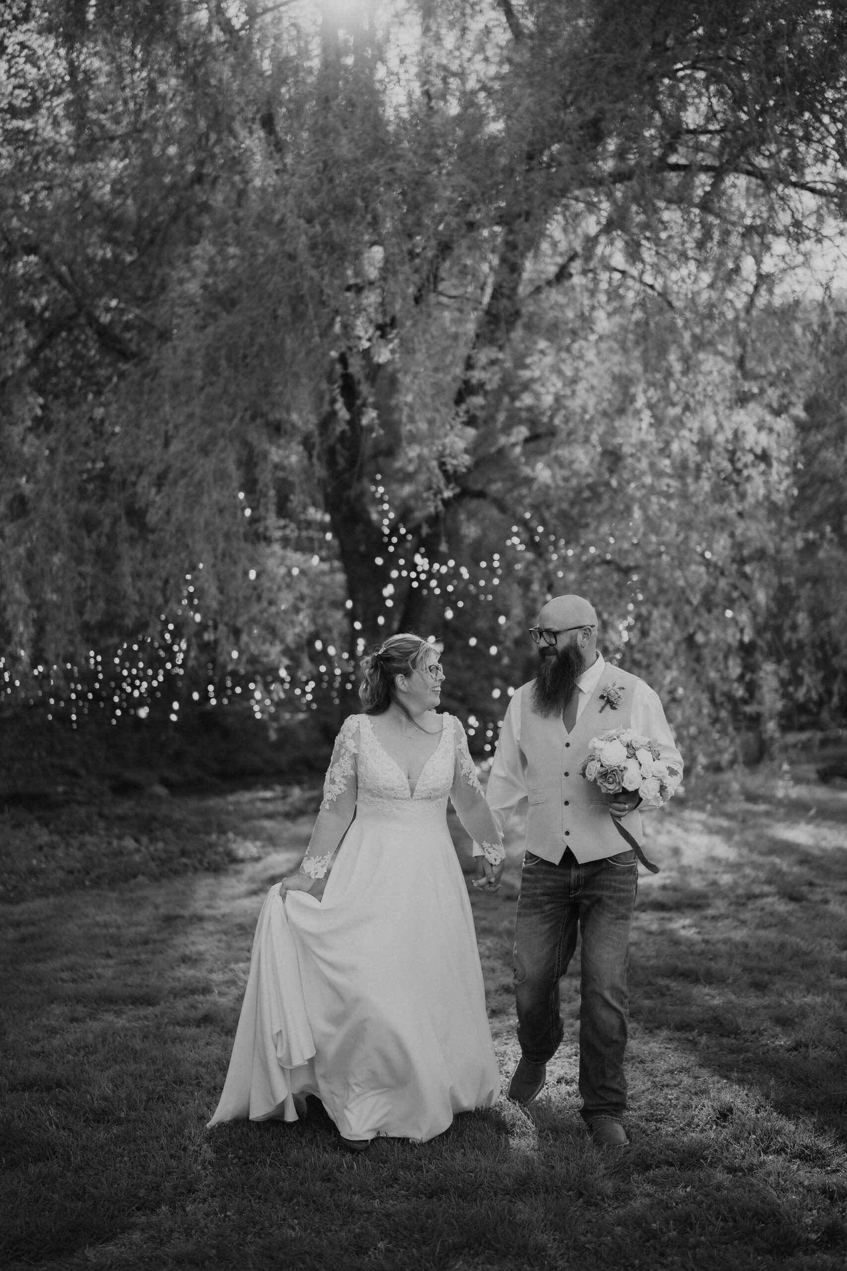 black and white candid wedding photo of bride and groom holding hands an walking through a willow tree for their gatlinburg elopement