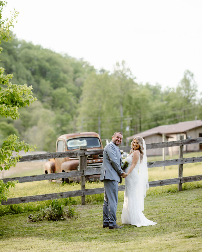 Bride and groom holding hands beside a rustic fence and vintage truck at Honeysuckle Hills, a picturesque Gatlinburg wedding venue.