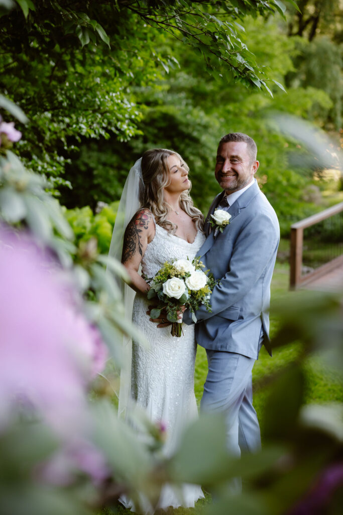 Bride and groom posing beneath lush greenery and blooming flowers at Honeysuckle Hills, with portraits captured by a smoky mountain elopement photographer.