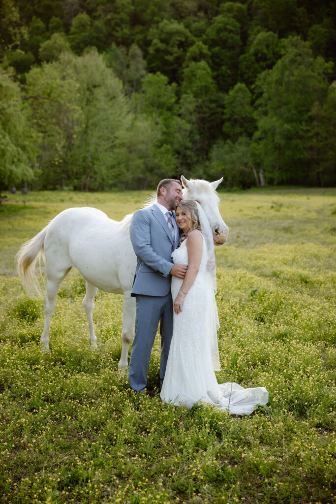 Bride and groom standing beside a white horse in a wildflower meadow at Honeysuckle Hills, a scenic Gatlinburg wedding venue perfect for intimate wedding portraits.