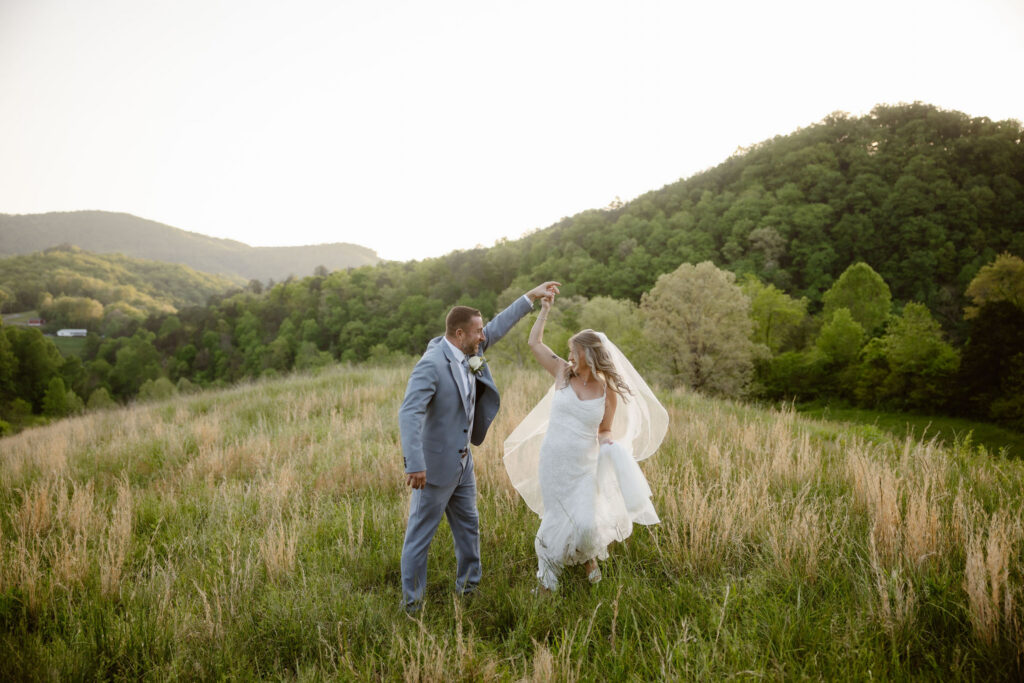 Groom twirling the bride in a mountain meadow at Honeysuckle Hills, with scenic views captured by a smoky mountain elopement photographer.