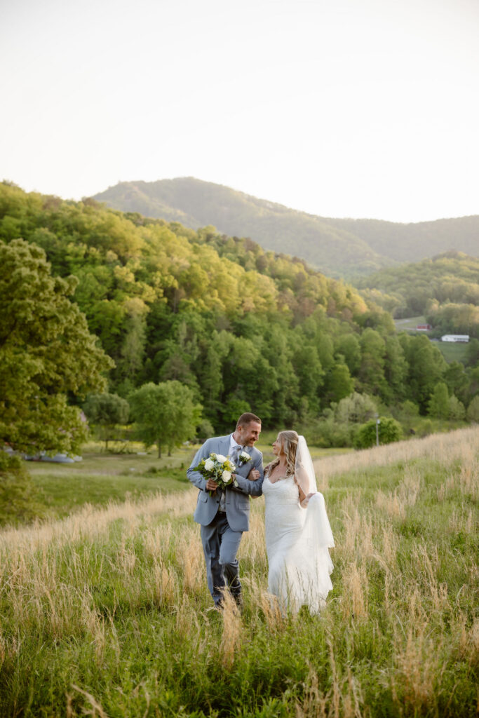 Newlyweds walking through a grassy hillside with Smoky Mountain views behind them, photographed by a smoky mountain elopement photographer.