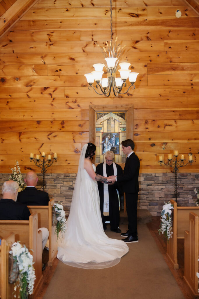 Couple exchanges rings during their ceremony inside one of the intimate Gatlinburg chapels, surrounded by warm wood walls, floral pew decorations, and stained glass.