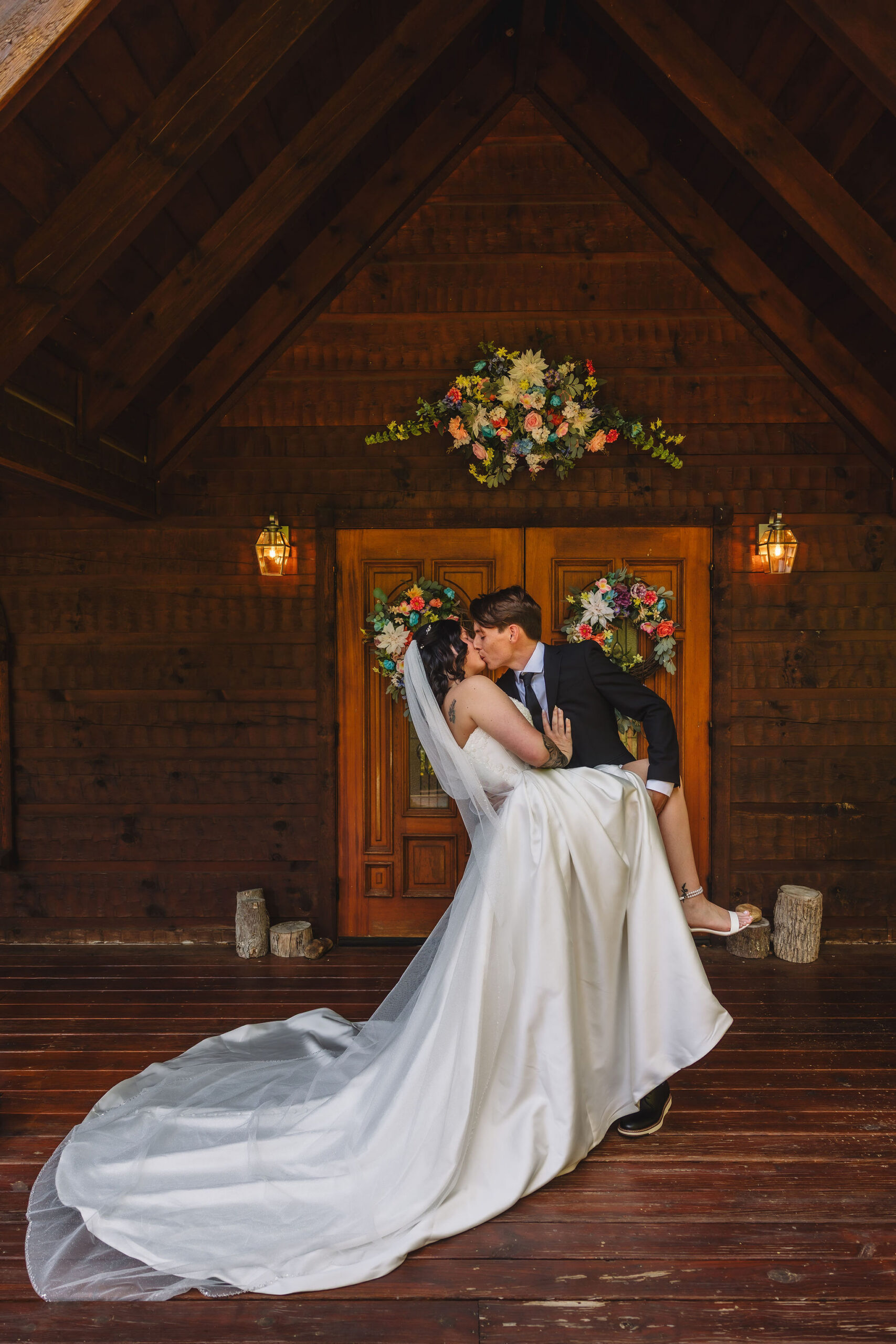 Newlyweds share a playful dip and kiss beneath colorful floral wreaths outside the Little Log Chapel in Gatlinburg after their intimate ceremony.