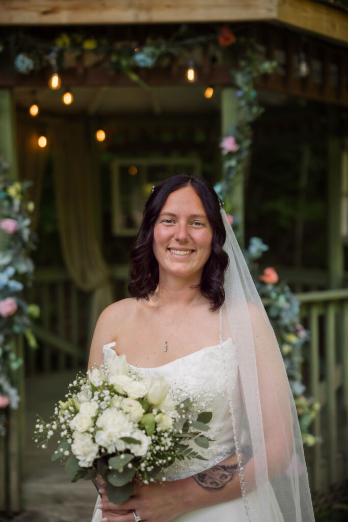 Bride holding a white rose bouquet in front of a flower-covered gazebo during a Gatlinburg elopement at the Little Log Chapel in Gatlinburg.