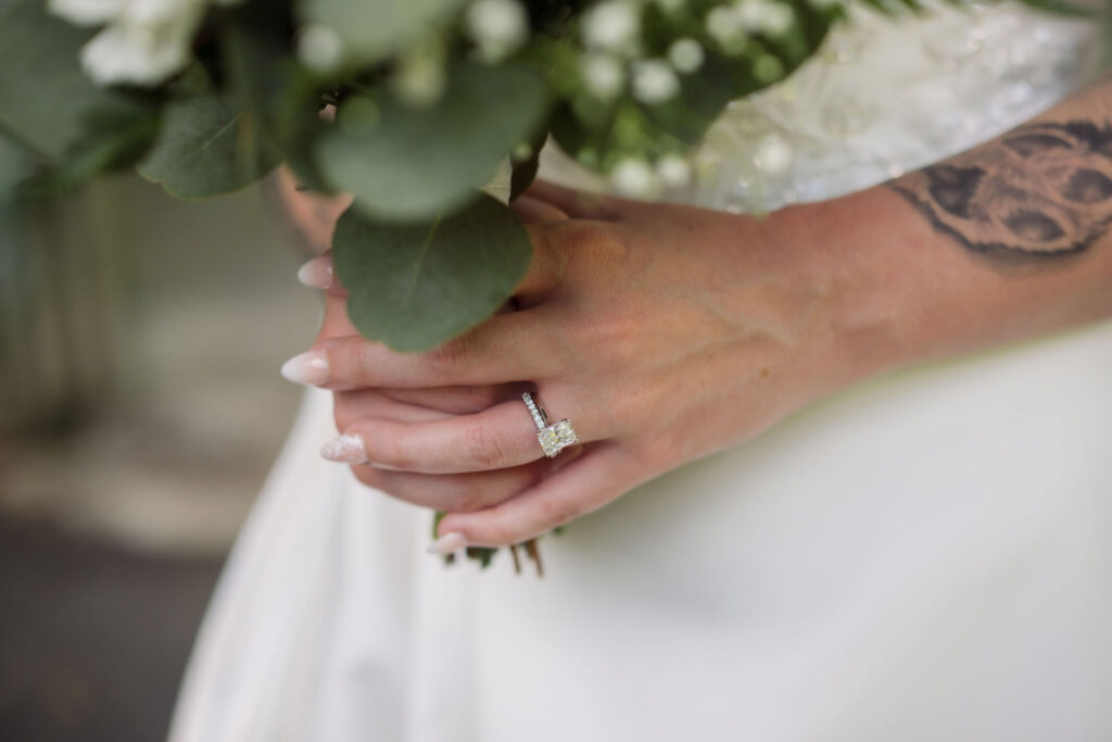 Close-up of the bride’s engagement ring and tattooed arm as she holds her greenery-filled bouquet during a Gatlinburg elopement.
