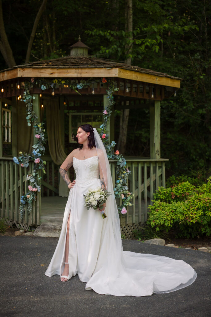 Bride in a white wedding gown and long veil poses with her bouquet beside a floral gazebo at one of the scenic Gatlinburg wedding venues.