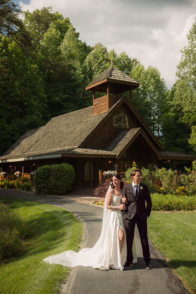 Newlyweds pose on the chapel path with the rustic Little Log Chapel in Gatlinburg and surrounding greenery behind them.