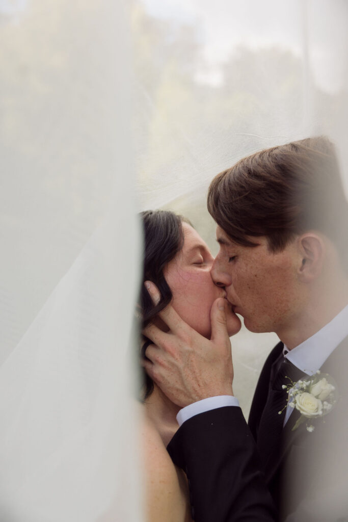 Newlyweds share a close-up kiss beneath the bride’s veil during their Gatlinburg elopement at the Little Log Chapel in Gatlinburg.