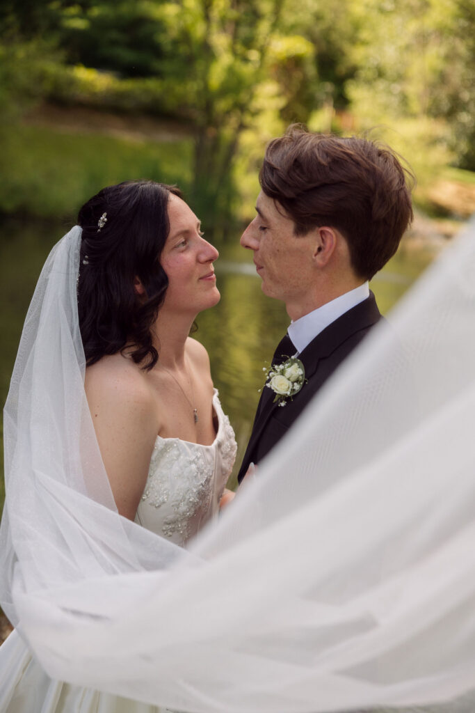 Bride and groom face each other beside a pond, framed by the bride’s flowing veil during portraits at one of the scenic Gatlinburg wedding venues.
