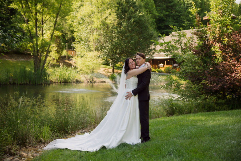 Newlyweds embrace beside a landscaped pond and fountain at the Little Log Chapel in Gatlinburg, surrounded by lush greenery after their Gatlinburg elopement.