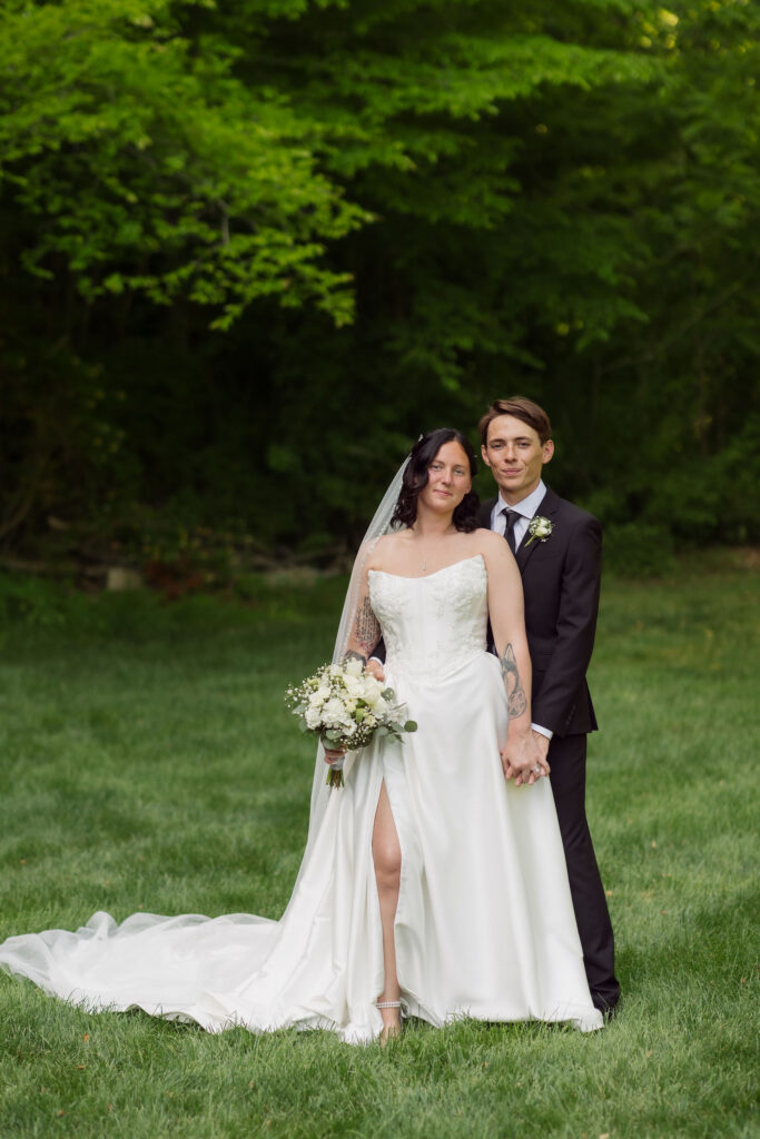 Bride holding a white floral bouquet poses with her partner on a grassy lawn during their Gatlinburg elopement.