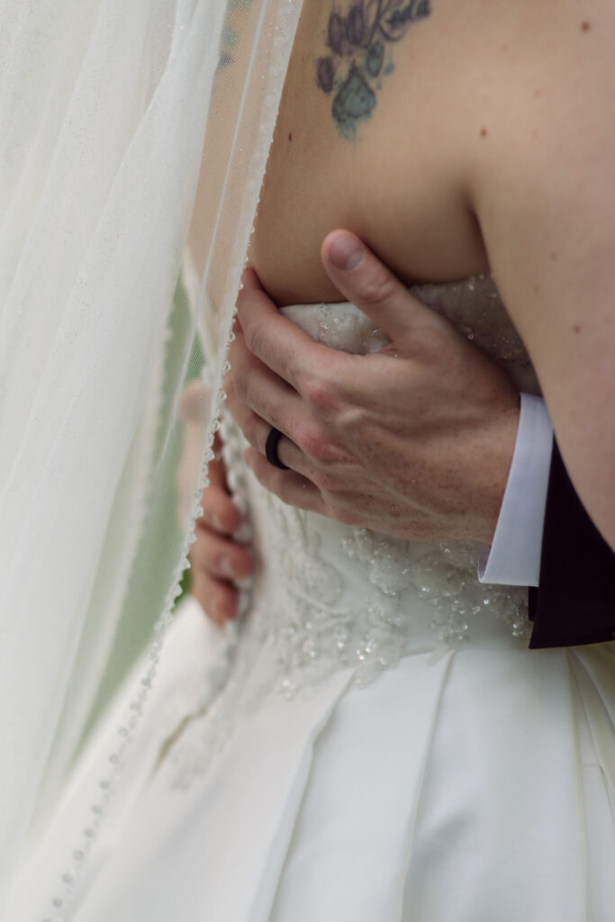 Close-up wedding portrait of the groom’s hand around the bride’s waist, highlighting her beaded gown and veil at one of the Gatlinburg chapels.