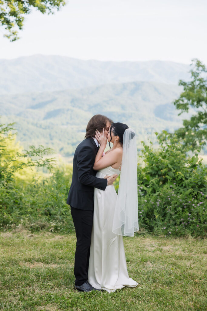 Bride and groom share a kiss surrounded by greenery and sweeping mountain views during their Foothills Parkway elopement.