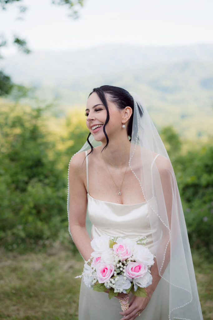 Bride holding a pink and white bouquet poses with mountain views behind her during a Foothills Parkway elopement.