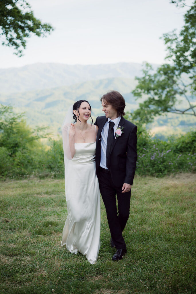 Bride and groom walk together through a grassy mountain overlook during their Gatlinburg elopement, surrounded by Smoky Mountain scenery.