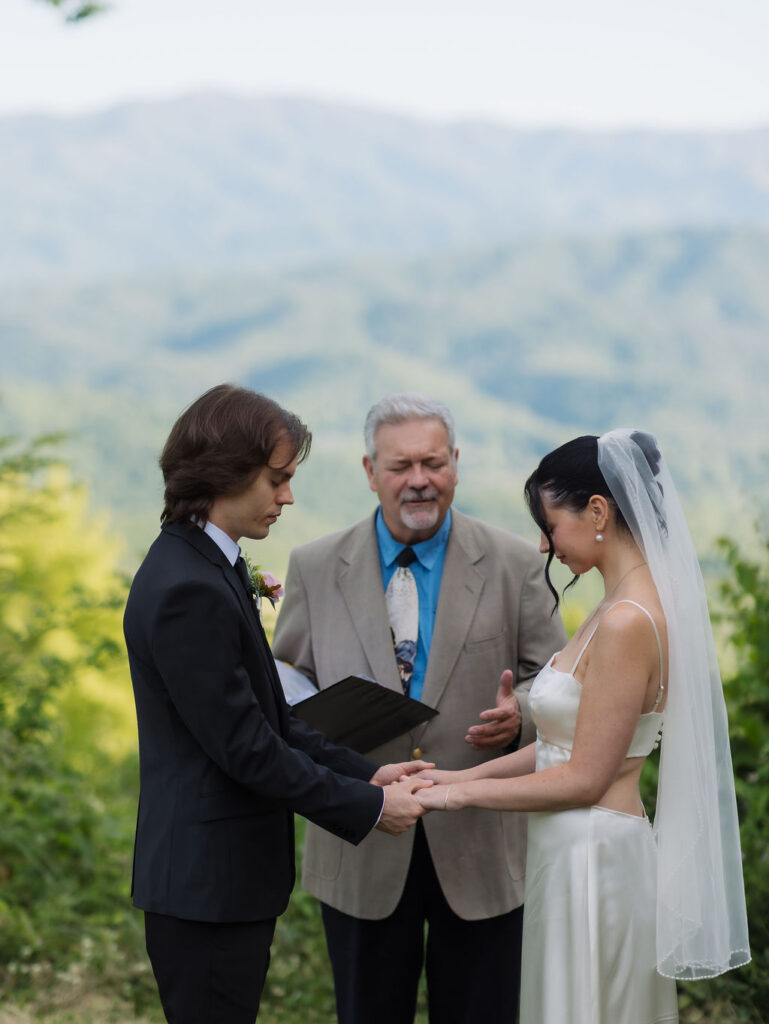 Bride and groom hold hands during their outdoor ceremony overlooking the mountains, capturing the scenery of eloping to Gatlinburg.