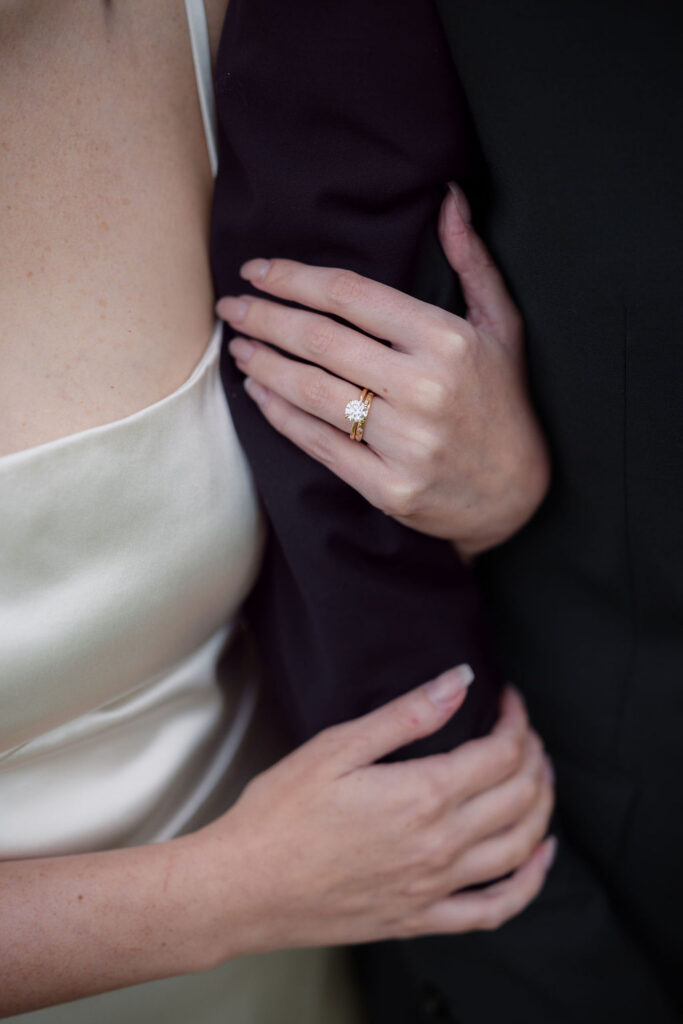 Close-up of the bride’s wedding and engagement rings as she holds the groom’s arm during their Foothills Parkway elopement.