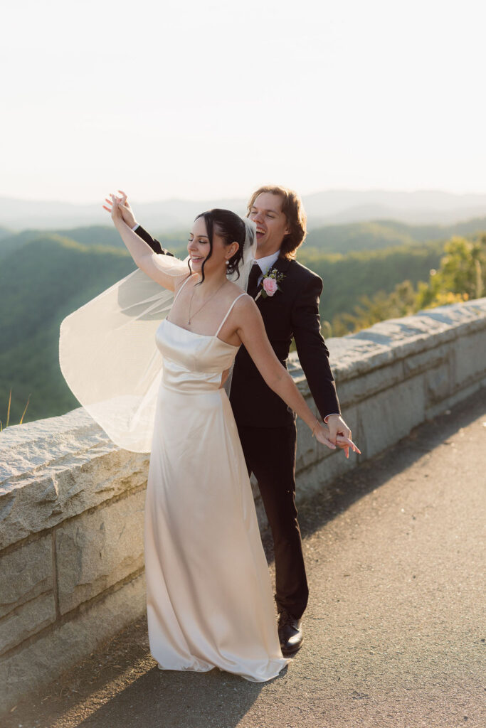 Newlyweds twirl beside the stone overlook on Foothills Parkway at golden hour, surrounded by sweeping Smoky Mountain views during their Gatlinburg elopement.