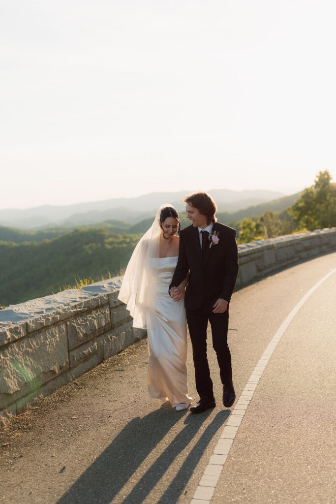 Newlyweds walk hand in hand along Foothills Parkway at golden hour with layered Smoky Mountain views behind them during their Gatlinburg elopement.