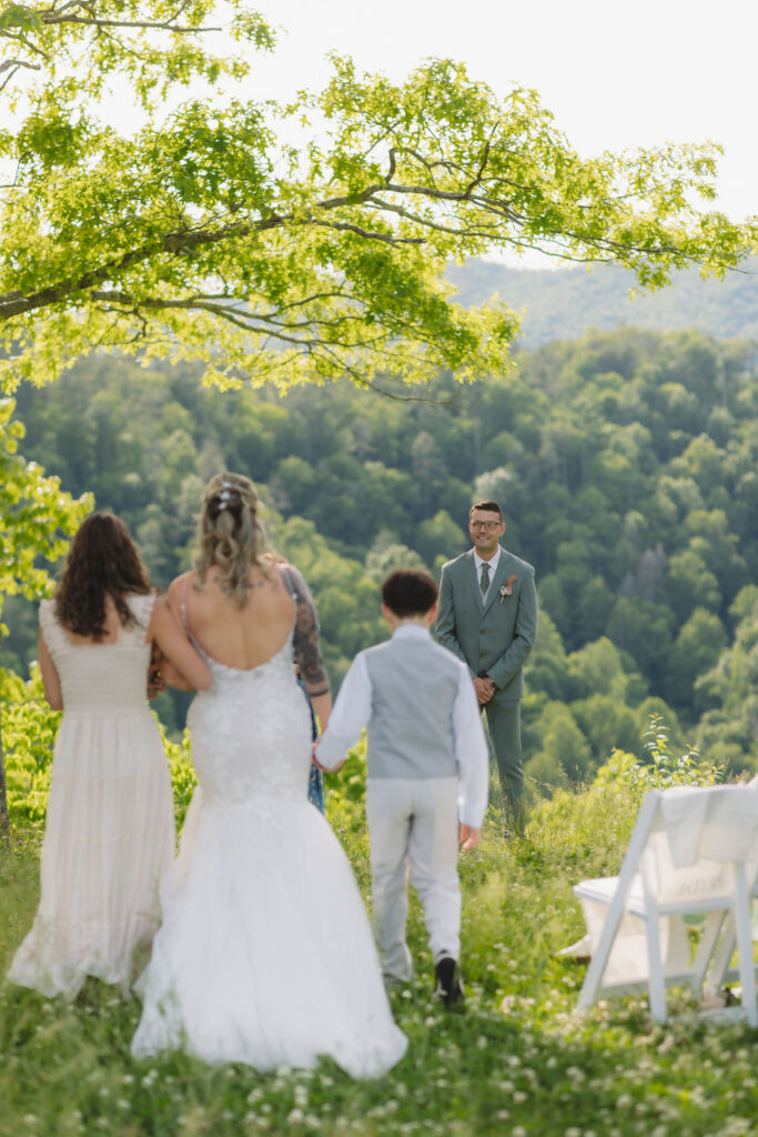 Bride walks toward the groom with two young attendants during an outdoor Gatlinburg elopement overlooking the Smoky Mountains.