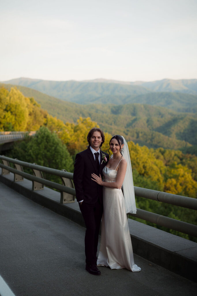 Bride and groom pose along Foothills Parkway with sweeping Smoky Mountain views behind them during their Gatlinburg elopement.