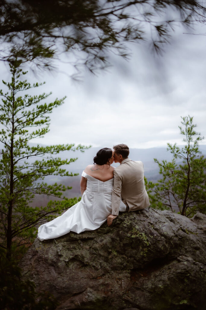 Couple sits together on a rocky overlook during their adventure of eloping to Gatlinburg at foothills parkway surrounded by mountain scenery.