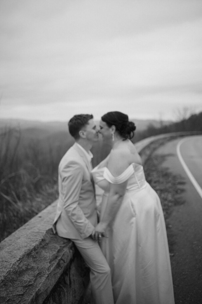 Couple shares a kiss beside the stone overlook during their adventure of eloping to Gatlinburg and foothills parkway with misty mountain views in the background.