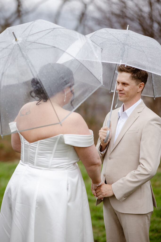 Couple smiles and holds hands beneath clear umbrellas during a rainy ceremony while eloping to Gatlinburg at foothills parkway.