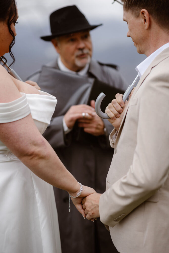 Close-up of a couple holding hands as an officiant leads their rainy ceremony while eloping to Gatlinburg at foothills parkway.