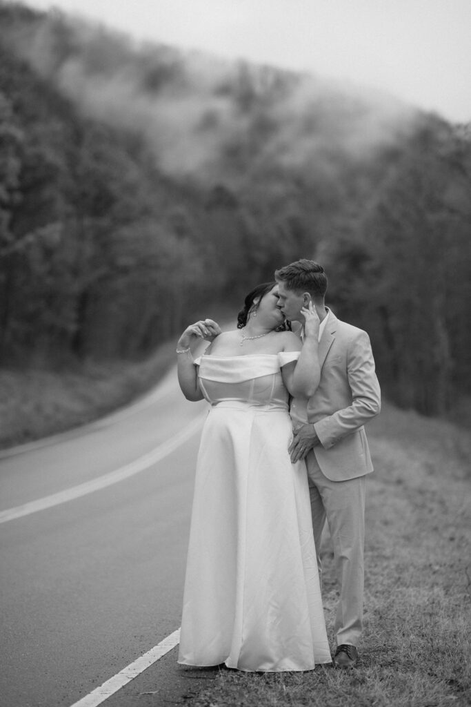 Newlyweds share a kiss along a quiet mountain road while eloping to Gatlinburg at foothills parkway.